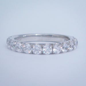 May include: A silver band with a row of small, round, clear diamonds.