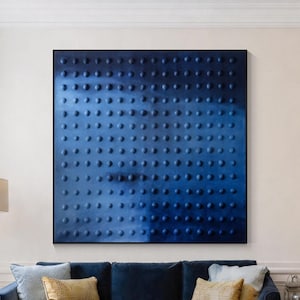 May include: A large square wall art piece featuring a deep navy blue surface with a uniform grid of raised circular bumps. The artwork is displayed on a light-colored wall above a dark blue velvet sofa in a living room setting.