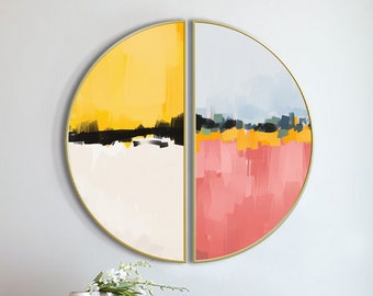 May include: A pair of abstract paintings in a circular shape with a gold frame. The paintings are divided in half, with one side featuring yellow, white, and black colors and the other side featuring pink, blue, and green colors. The paintings are hanging on a white wall above a dark brown wooden console table with gold accents.