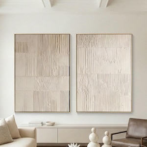 Puede incluir: Dos grandes piezas de arte mural rectangular con una superficie texturizada de color blanco roto, patrones de costillas verticales y secciones lisas. La obra está enmarcada en madera fina de color claro y expuesta en una pared blanca.