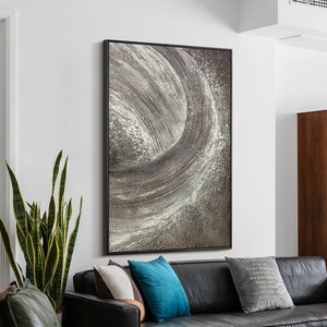 May include: A black leather sofa with three pillows, a green plant, and a gray and white abstract painting on the wall behind it.