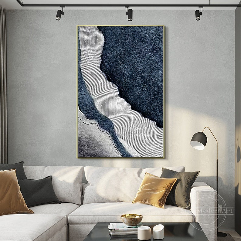 Pu&ograve; includere: Un'opera d'arte da parete rettangolare verticale caratterizzata da una composizione astratta con aree testurizzate blu navy profondo e una sezione bianca a contrasto con sottili linee curve parallele. Sottile cornice dorata.
