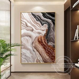 Könnte beinhalten: Abstrakter Kunstdruck mit goldenem Rahmen. Das Kunstwerk zeigt ein wirbelndes Design in Braun-, Schwarz- und Weißtönen mit einem strukturierten, glitzernden Effekt. Das Gemälde wird in einem modernen Innenraum gezeigt.