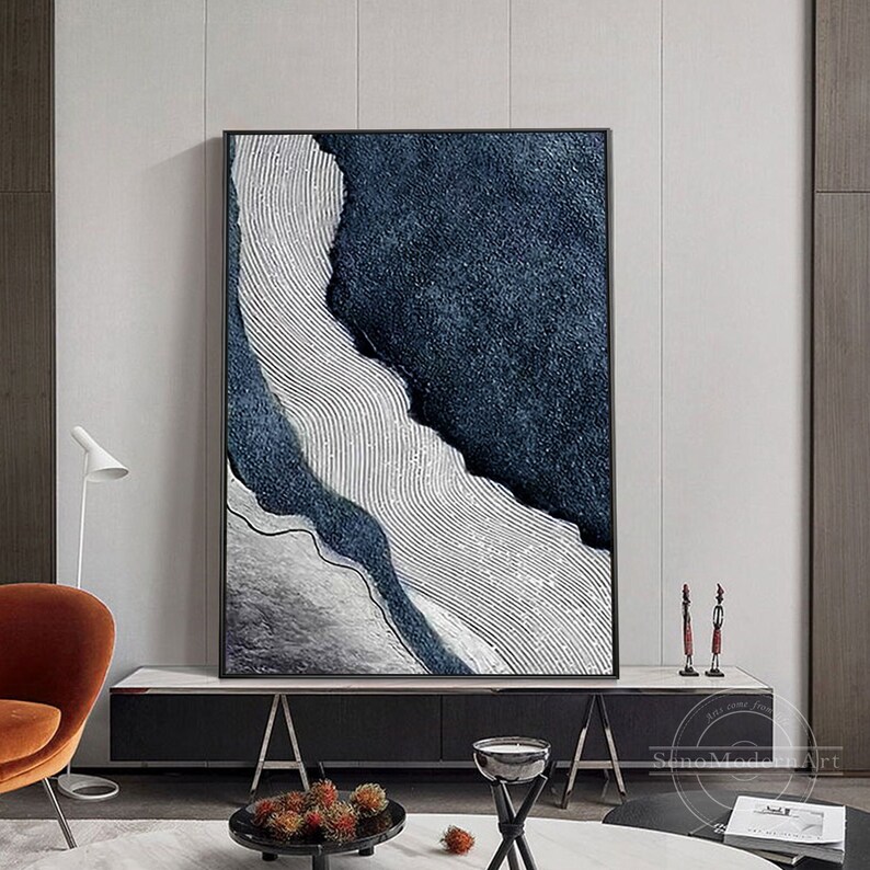 Pu&ograve; includere: Un'opera d'arte murale rettangolare con una composizione astratta testurizzata. L'opera presenta sezioni blu navy profondo con una superficie granulare contrastate da un'area chiara caratterizzata da sottili linee ondulate parallele.