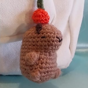 May include: A small crocheted brown animal with an orange pom-pom on top. The animal is hanging from a black string.