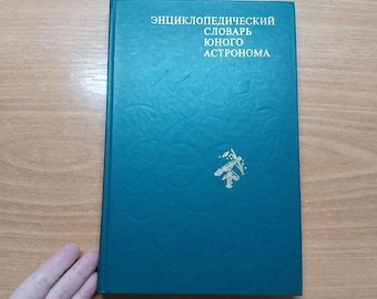 Könnte beinhalten: Ein türkisfarbenes Buch mit dem Titel "Энциклопедический словарь юного астронома" in weißer Schrift. Auf dem Einband befindet sich eine goldene Illustration eines Teleskops. Das Buch ist geschlossen und in gutem Zustand.