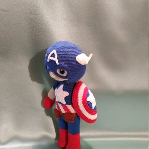 May include: A crocheted Captain America doll with a blue and red costume, a white star on the chest, and a red, white, and blue shield.
