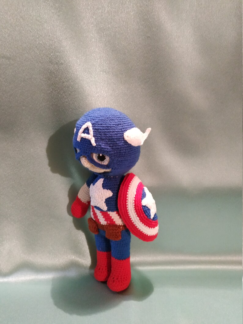 May include: A crocheted Captain America doll with a blue and red costume, a white star on the chest, and a red, white, and blue shield.