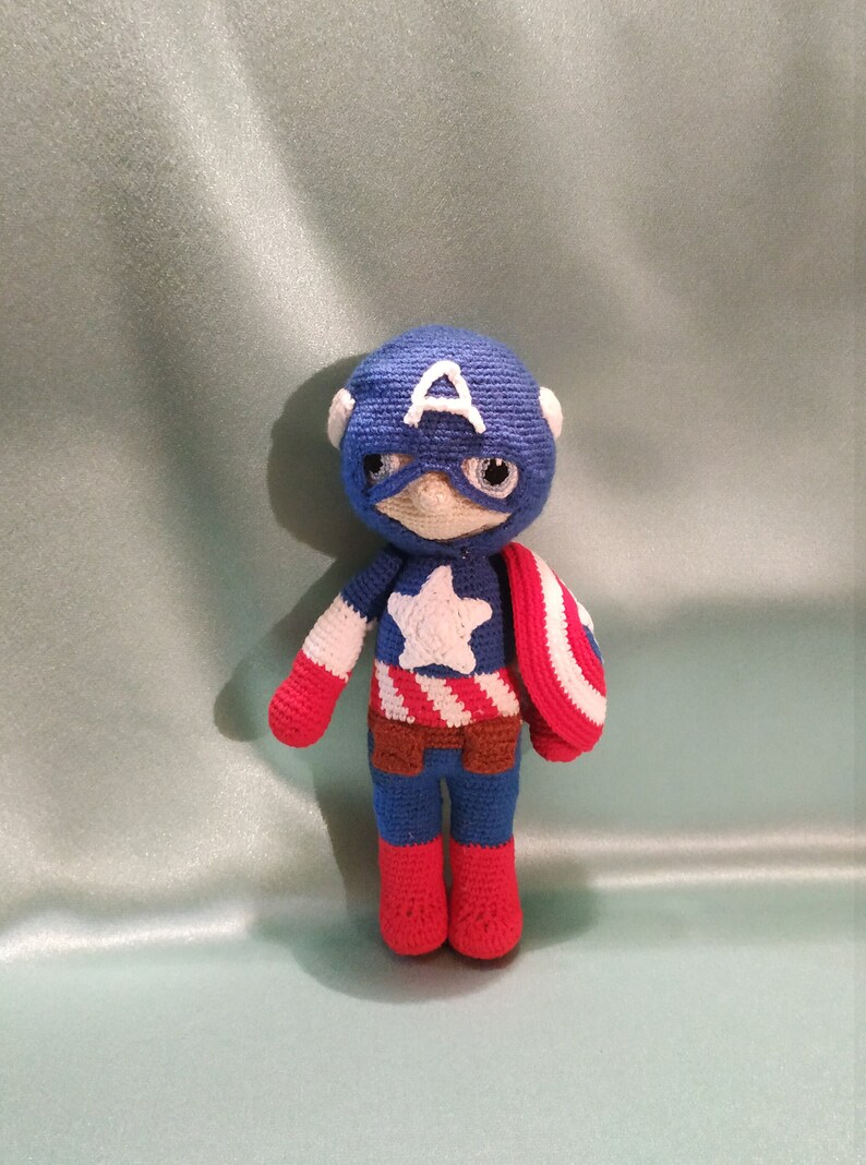 May include: A crocheted Captain America doll with a blue and red costume, a white star on the chest, and a red and white shield.