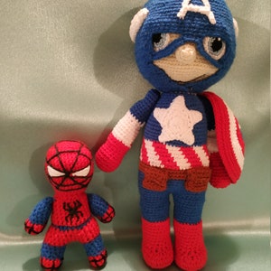 May include: Two crocheted superhero toys. Captain America is wearing a blue and red costume with a white star and a red, white, and blue shield. Spiderman is wearing a red and blue costume with a black spider on the chest.
