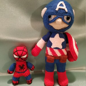 May include: Two crocheted superhero toys. Captain America is wearing a blue, red, and white costume with a red, white, and blue shield. Spiderman is wearing a red and blue costume with a black spider on the chest.