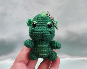 May include: Green crocheted monster keyring with black eyes. The monster has a green and white striped pattern on its body.