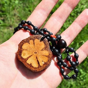Può includere: Collana con pendente in legno fatto a mano. Il pendente marrone chiaro presenta un motivo floreale intagliato. La collana ha una catena di perline nere. Il pendente misura circa 4 cm di diametro.