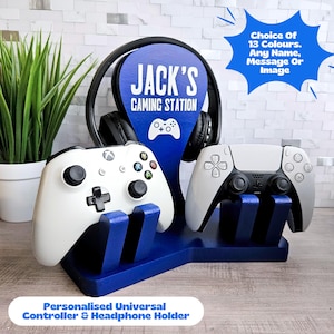 Op de afbeelding: Een blauwe houten standaard met de tekst "JACK'S GAMING STATION" en een ruimte voor koptelefoons. De standaard heeft ook twee slots voor controllers, een voor een Xbox-controller en een voor een Playstation-controller.