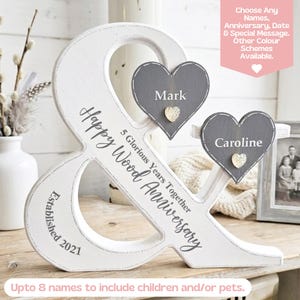 May include: A white wooden ampersand sign featuring the text "5 Glorious Years Together Happy Wood Anniversary" and "Established 2021". Two grey heart-shaped wooden plaques are attached, labelled "Mark" and "Caroline" with small gold hearts.