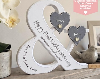 May include: A white wooden ampersand-shaped anniversary decoration. It features two gray heart-shaped plaques with names, and text that reads "Happy Pearl Wedding Anniversary" and "30 Wonderful Years Together!" The date "Est 17th June 1996" is also included.