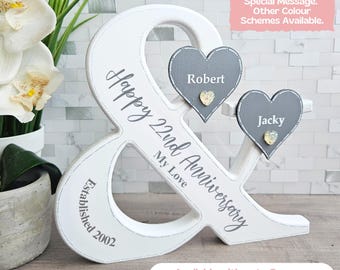 Puede incluir: Un letrero de madera blanco en forma de ampersand con dos corazones grises, uno con el nombre "Robert" y el otro con el nombre "Jacky". El letrero dice "Happy 22nd Anniversary My Love Established 2002".