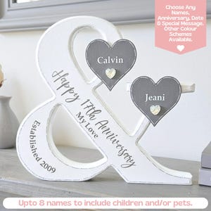 May include: A white wooden ampersand sign featuring the text Happy 17th Anniversary My Love and Established 2009. Two grey heart-shaped plaques are attached, each displaying a name, Calvin and Jeani, with a small decorative crystal heart.