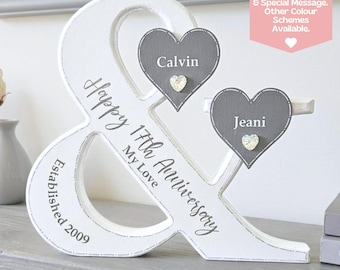 May include: A white wooden ampersand sign featuring the text Happy 17th Anniversary My Love and Established 2009. Two grey heart-shaped plaques are attached, each displaying a name, Calvin and Jeani, with a small decorative crystal heart.
