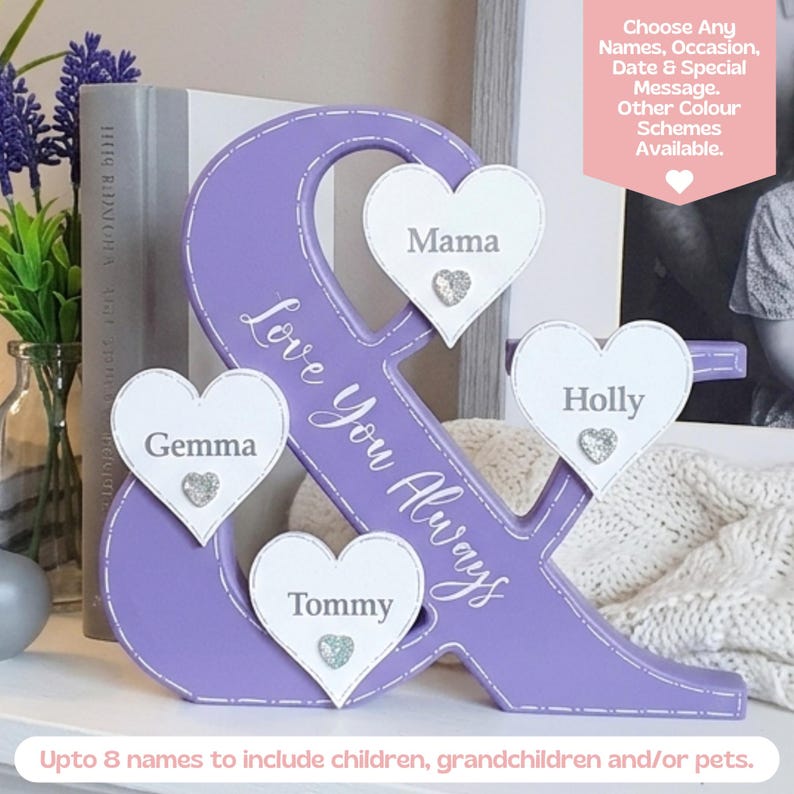 May include: A purple wooden ampersand sign featuring the white text Love You Always and four white heart-shaped plaques with the names Mama, Gemma, Tommy, and Holly. Each heart includes a small silver glittery heart accent at the bottom.
