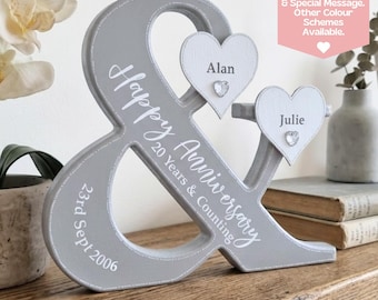 Puede incluir: Una decoración de aniversario en forma de & de madera gris con las palabras "Happy Anniversary 20 Years & Counting" y "23rd Sept 2006". Dos corazones blancos están adjuntos, cada uno con un nombre y una gema. También es visible el texto "Choose Any Names, Anniversary, Date & Special Message. Other Colour Schemes Available."