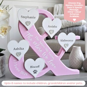 May include: A pink ampersand-shaped wooden display featuring four white heart-shaped plaques with the names Stephanie, Anisha, Aishwarya, Ashika, and Biscoff with a paw print. The text reads The More We Grow, The More We Love and 17 June 2024.