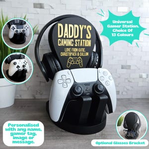May include: A black and white gaming console controller stand with a personalized plaque that says "Daddy's Gaming Station Love from Katie, Christopher & Callum". The stand has a headset holder and an optional glasses bracket.