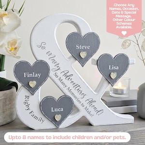 May include: A white wooden ampersand sign featuring the text So Many Adventures Ahead! So Many Memories to Make! and Rigby Family. Four grey heart-shaped plaques are attached, each displaying a name: Finlay, Luca, Steve, and Lisa.