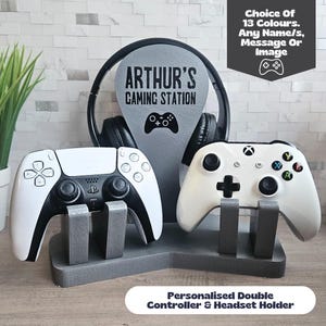 May include: A personalised double controller and headset holder in grey. The holder features a stand for two game controllers and a headset rest with the text "ARTHUR'S GAMING STATION". The image also includes the text "Choice Of 13 Colours. Any Name/s, Message Or Image".