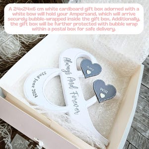 May include: A white ampersand-shaped wooden sign with the text Always And Forever and 22nd June 2024 printed on it. Two dark grey heart-shaped attachments are fixed to the sign, each featuring a small white heart and the names Amy and Will.