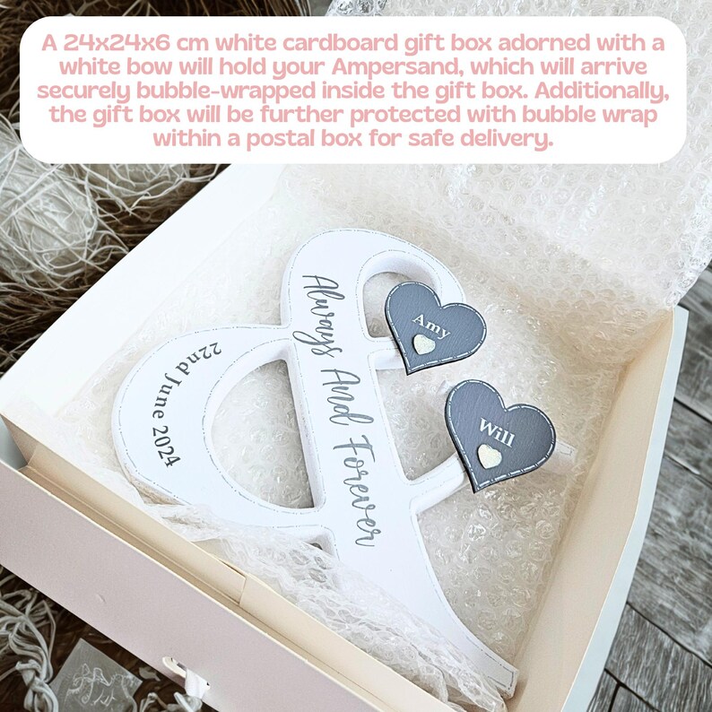 May include: A white ampersand-shaped wooden sign with the text Always And Forever and 22nd June 2024 printed on it. Two dark grey heart-shaped attachments are fixed to the sign, each featuring a small white heart and the names Amy and Will.