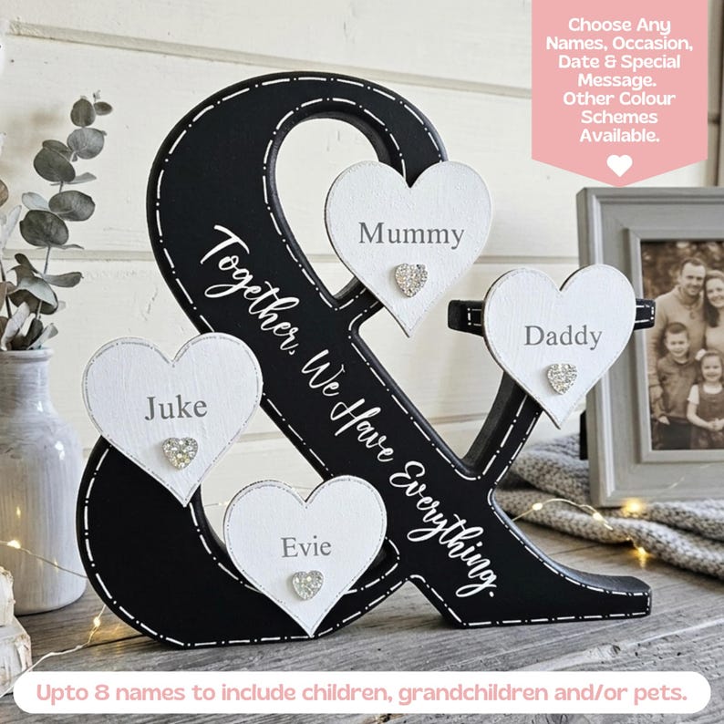 May include: A black ampersand-shaped wooden sign featuring white heart-shaped plaques with the names Mummy, Daddy, Juke, and Evie. The sign includes the text Together, We Have Everything and small decorative crystal hearts on each plaque.