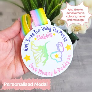May include: A white, round, personalised medal with a rainbow ribbon. The medal features a colourful illustration of a fairy and a toilet with the text "Well Done for Using the Potty Isabelle Love Mummy & Daddy xx".