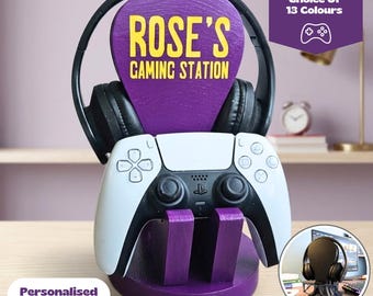 Może przedstawiać: Fioletowy drewniany stojak do gier z żółtym napisem ROSE'S GAMING STATION. Stojak podtrzymuje czarne słuchawki nauszne oraz biało-czarny kontroler do gier. Tekst na obrazie zawiera Universal Gamer Stand Choice Of 13 Colours oraz Personalised with any name and message.