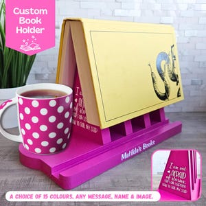 Puede incluir: Un soporte para libros rosa con un libro amarillo apoyado en él. El soporte para libros tiene una ranura para un libro y un pequeño estante para una taza. El soporte para libros tiene el texto "Matilda's Books" en la parte delantera. La taza es rosa con lunares blancos. El libro tiene el texto "No tengo miedo de las tormentas, estoy aprendiendo a navegar mi barco" en la parte delantera.