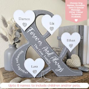 May include: A grey ampersand-shaped wooden display piece featuring white heart-shaped plaques with the names Darren, Liz, Ethan, and Lara. The text Forever And Always and The Gray Family is printed on the grey surface, along with the words Stronger Together.