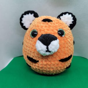 May include: A crocheted tiger plush toy with orange fur, black stripes, white accents, and green eyes.