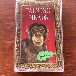 May include: A cassette tape case featuring the album cover for Talking Heads' "Naked." The cover art displays a chimpanzee against a red background, with the band's name at the top and the album title on a green leaf.
