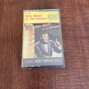 May include: A vintage cassette tape of Bill Haley & The Comets' "Everest Golden Greats" album. The cassette features a photo of Bill Haley and the album title. The cassette is in a clear plastic case and is labeled "Dolby Everest Compatible Cassette."
