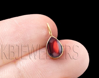 Puede incluir: Un colgante en forma de lágrima con una piedra preciosa roja engastada en un marco de oro.