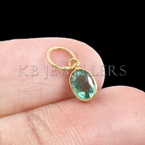 May include: A gold pendant with a green oval emerald gemstone. The pendant has a simple loop for attaching to a chain.