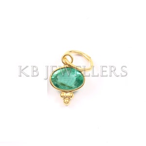 May include: A gold pendant with a green oval gemstone and a small gold loop at the top. The pendant has three small gold balls hanging from the bottom.