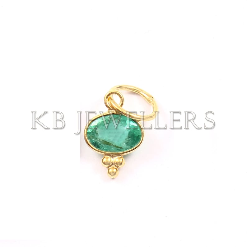 May include: A gold pendant with a green oval gemstone and a small gold loop at the top. The pendant has three small gold balls hanging from the bottom.