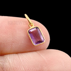 May include: A gold pendant with a purple amethyst gemstone. The pendant is rectangular in shape and has a simple design.