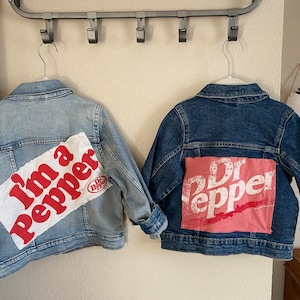 Pode incluir: Duas jaquetas de ganga com patches de Dr Pepper. Uma jaqueta tem um patch branco com texto vermelho que diz "I'm a Pepper" e a outra tem um patch rosa com texto branco que diz "Dr Pepper".