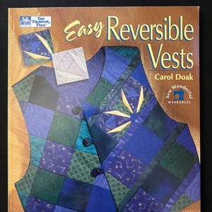 May include: A book cover titled "Easy Reversible Vests" by Carol Doak. The cover features a quilted vest in shades of blue and green, with star-like accents. The book is from "That Patchwork Place" and includes the words "Sew Wonderful Wearables."