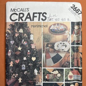 May include: McCall's Crafts pattern envelope featuring a Christmas tree decorated with handmade ornaments. The cover includes various craft projects, such as dolls, hearts, and a house. The text "Marti Michell" is visible.