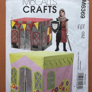 May include: McCall's Crafts sewing pattern M6369 featuring two children's playhouses. One is designed as a castle with gray walls, red roof, and yellow flags. The other is a pink and green house with flower accents.