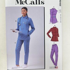 May include: McCall's M8468 sewing pattern envelope for scrubs, size AA (XS-S-M). The front shows a model in a blue zip-up jacket and matching pants, with illustrations of three garment views labeled A, B, and C in purple, red, and blue.