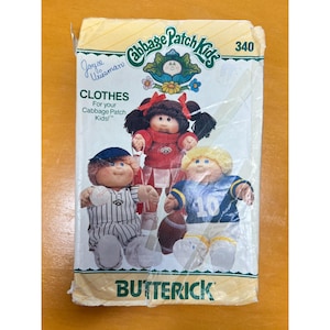 May include: A Butterick Cabbage Patch Kids sewing pattern envelope, number 340, featuring illustrations of three dolls wearing sports-themed outfits: a baseball uniform, a cheerleader costume, and a football jersey with the number 10.
